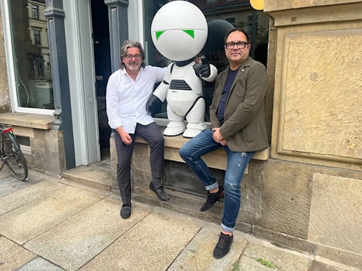 Frank Leichsenring (links) und Karsten Lehmann sitzen vor dem neuen Laden auf einem Fenstersims neben der Roboterfigur Marvin. Die weiße Roboterfigur dient als inoffizielles Maskottchen für den Whisky „Hellinger 42“.