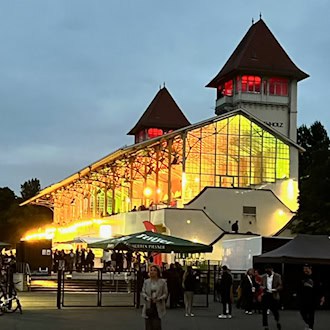 Abendliche Stimmung am Partyrenntag: Die beleuchtete Tribüne der Galopprennbahn Scheibenholz mit ihren markanten Türmen und lebhaftem Treiben vor dem Gebäude.