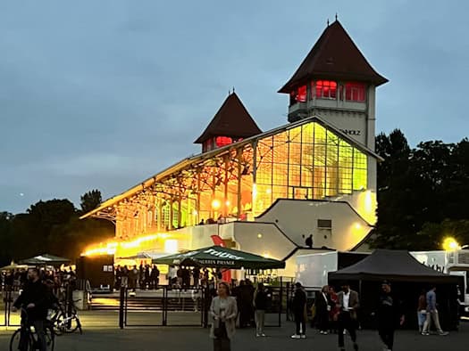 Abendliche Stimmung am Partyrenntag: Die beleuchtete Tribüne der Galopprennbahn Scheibenholz mit ihren markanten Türmen und lebhaftem Treiben vor dem Gebäude.