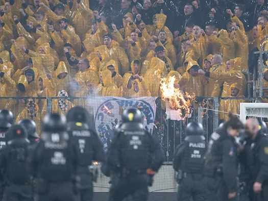 Dynamo Dresden-Fans im K-Block während der Ausschreitungen gegen Hertha BSC. Im Vordergrund sichern zahlreiche Polizeikräfte den Innenraum, während im Fanblock ein brennender Gegenstand zu sehen ist.
