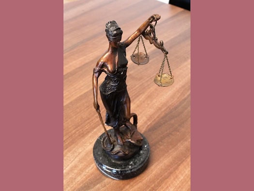 Eine kleine Bronze-Statue der Justitia mit Augenbinde, Waage und Schwert steht auf einer hölzernen Tischoberfläche. Das Symbolbild steht für die Anklage der Staatsanwaltschaft Dresden.