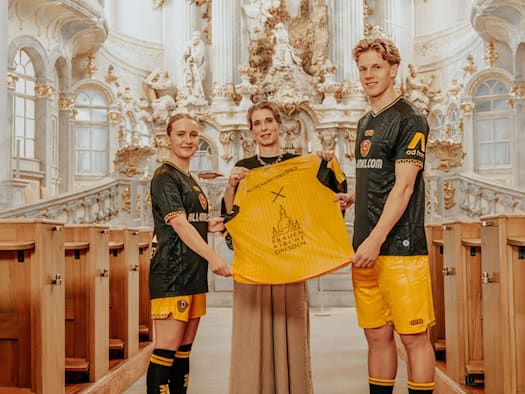 Jo-Anne Klinger, Maria Noth und Till Neininger (v.l.) präsentieren im barocken Innenraum der Dresdner Frauenkirche ein gelbes Dynamo-Sondertrikot, das die Logos des Fußballvereins und der Stiftung Frauenkirche Dresden verbindet.