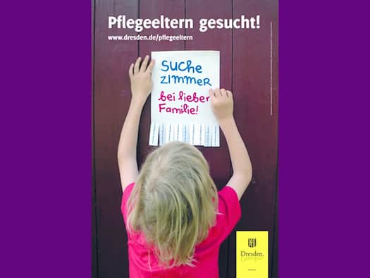 Informationsplakat der Stadt Dresden: Ein blondes Kind von hinten bringt einen Zettel an einer Holzwand an. Darauf steht in bunter Handschrift: „Suche Zimmer bei lieber Familie!“. Oben steht der Schriftzug „Pflegeeltern gesucht!“, unten das Logo der Stadt Dresden.