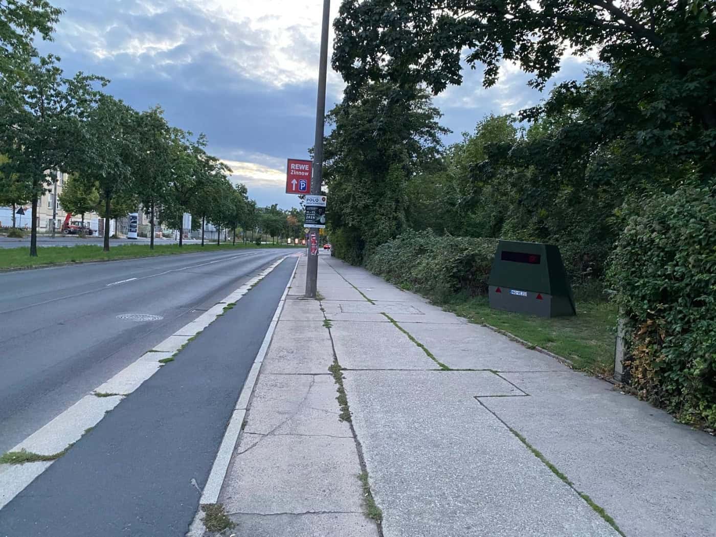 Straßenansicht des Zelleschen Wegs mit Gehweg und Radweg in Dresden. Am rechten Wegesrand steht vor grünem Gebüsch ein olivgrüner, trapezförmiger Blitzer-Anhänger mit dem Kennzeichen HWI-VE 213.