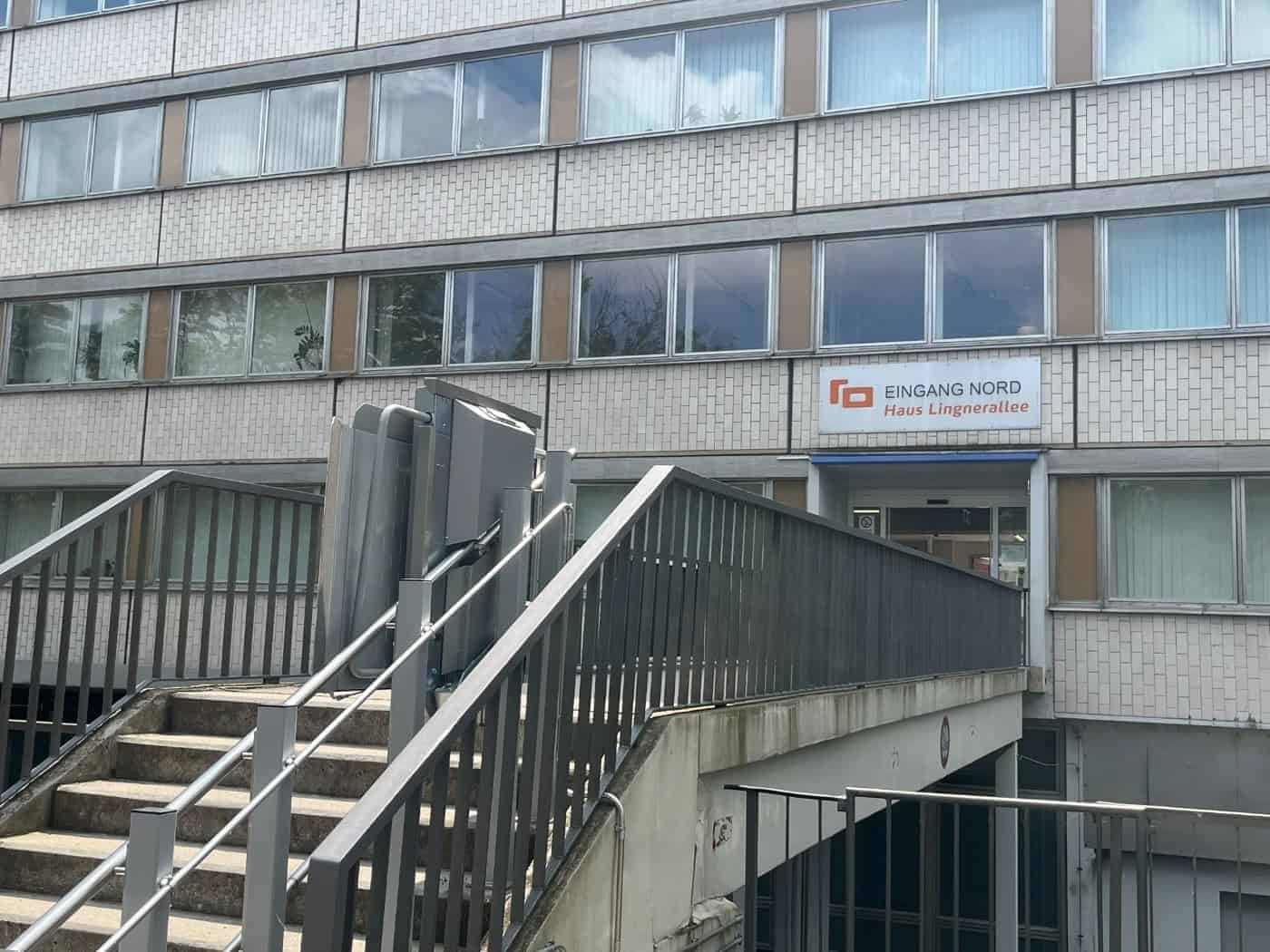 Treppenaufgang mit metallenem Rollstuhllift zum Gebäudeeingang mit dem Schild „EINGANG NORD Haus Lingnerallee“ an einem mehrstöckigen Verwaltungsgebäude in Dresden.