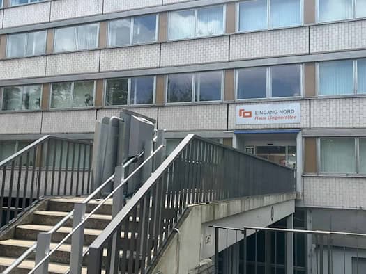 Treppenaufgang mit metallenem Rollstuhllift zum Gebäudeeingang mit dem Schild „EINGANG NORD Haus Lingnerallee“ an einem mehrstöckigen Verwaltungsgebäude in Dresden.
