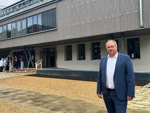 Dresdens Oberbürgermeister Dirk Hilbert steht im blauen Anzug auf dem geschotterten Vorplatz der neu gebauten Scheune. Im Hintergrund ist die Holzfassade des Kulturzentrums und der Eingang mit provisorischer Holztreppe zu sehen.