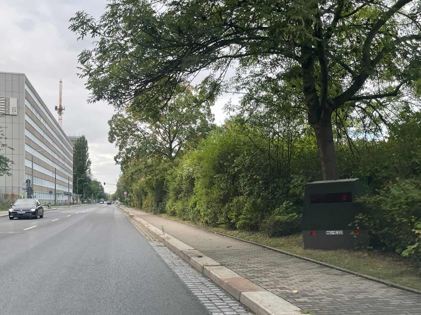 Blick aus der Perspektive eines Autofahrers auf die Strehlener Straße in Dresden: Am rechten Fahrbahnrand steht unter einem dichten Baum und vor einer Hecke der olivgrüne Messanhänger HWI-VE 213.