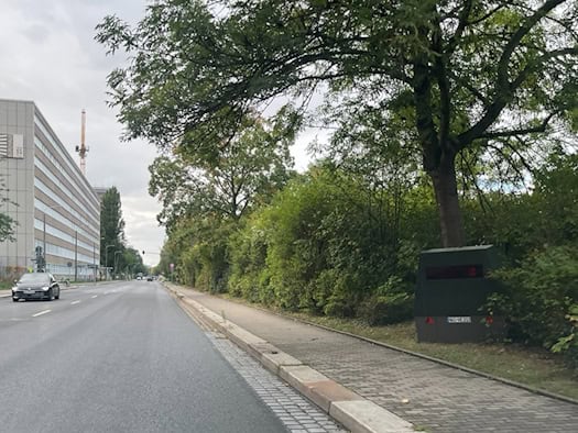 Blick aus der Perspektive eines Autofahrers auf die Strehlener Straße in Dresden: Am rechten Fahrbahnrand steht unter einem dichten Baum und vor einer Hecke der olivgrüne Messanhänger HWI-VE 213.