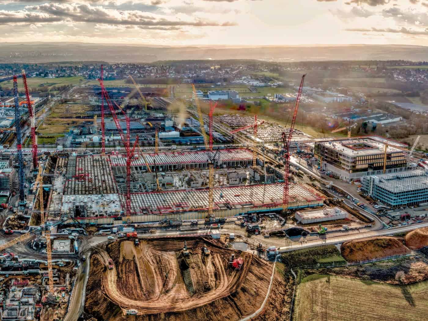 Luftaufnahme einer riesigen Großbaustelle für ein Chipwerk im Dresdner Norden. Zahlreiche rote und gelbe Baukräne stehen auf dem Areal mit Erdaushub und Rohbauten. Im Hintergrund sind angrenzende Felder und das Umland zu sehen.