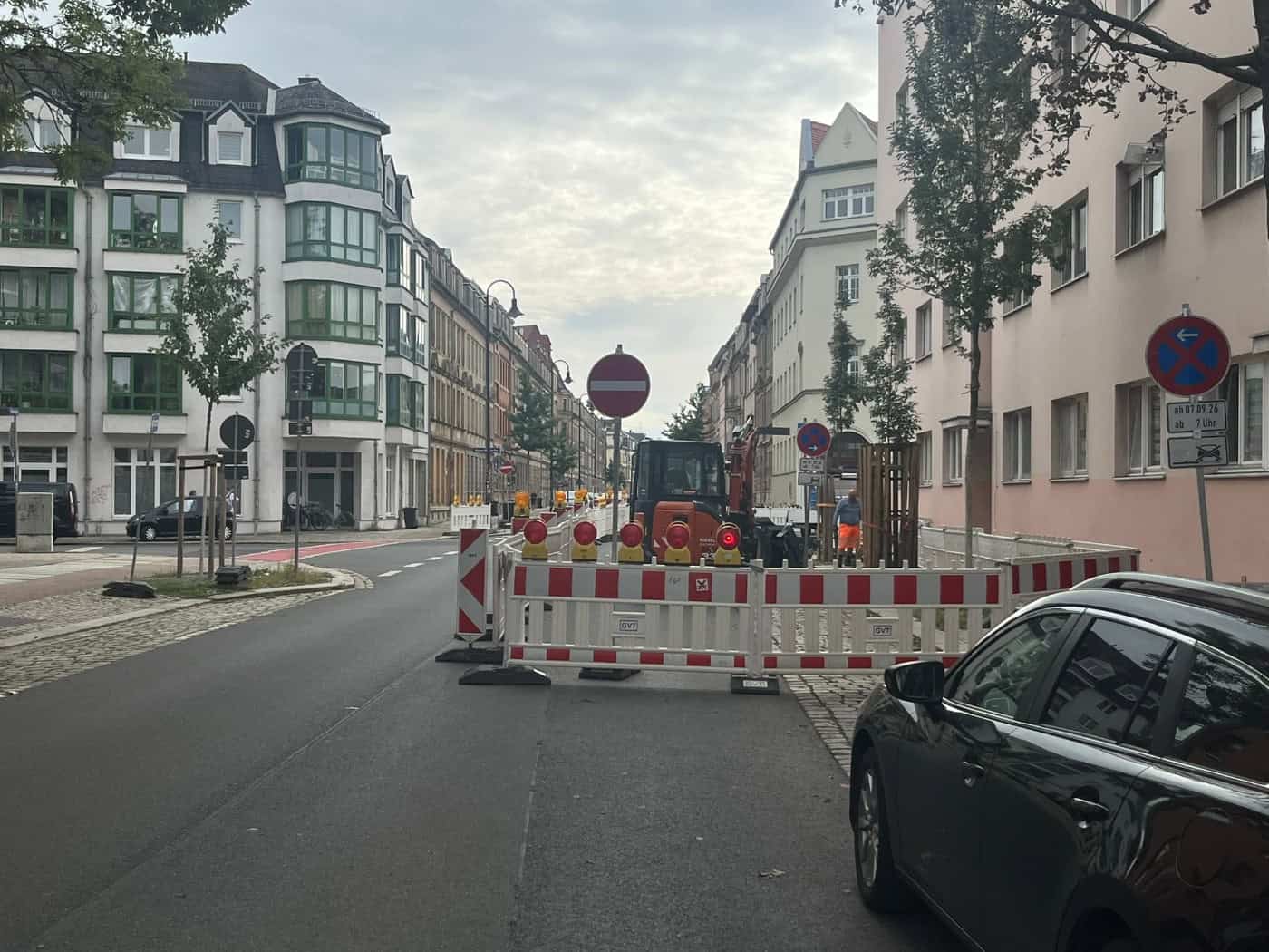 Straßenansicht in Dresden-Pieschen mit eingerichteter Baustelle: Rot-weiße Absperrgitter, ein kleiner orangefarbener Bagger und Verbotsschilder blockieren eine Fahrbahnseite der Rehefelder Straße zwischen mehrstöckigen Wohngebäuden.