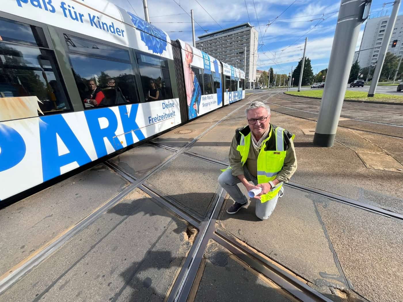 DVB-Infrastrukturchef Sandro Zimmermann kniet in Warnweste an den Schienen der Gleiskreuzung am Pirnaischen Platz in Dresden. Im Hintergrund fährt eine Straßenbahn über die Kreuzung.