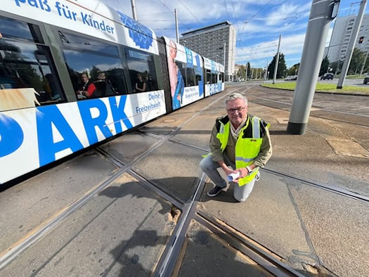 DVB-Infrastrukturchef Sandro Zimmermann kniet in Warnweste an den Schienen der Gleiskreuzung am Pirnaischen Platz in Dresden. Im Hintergrund fährt eine Straßenbahn über die Kreuzung.