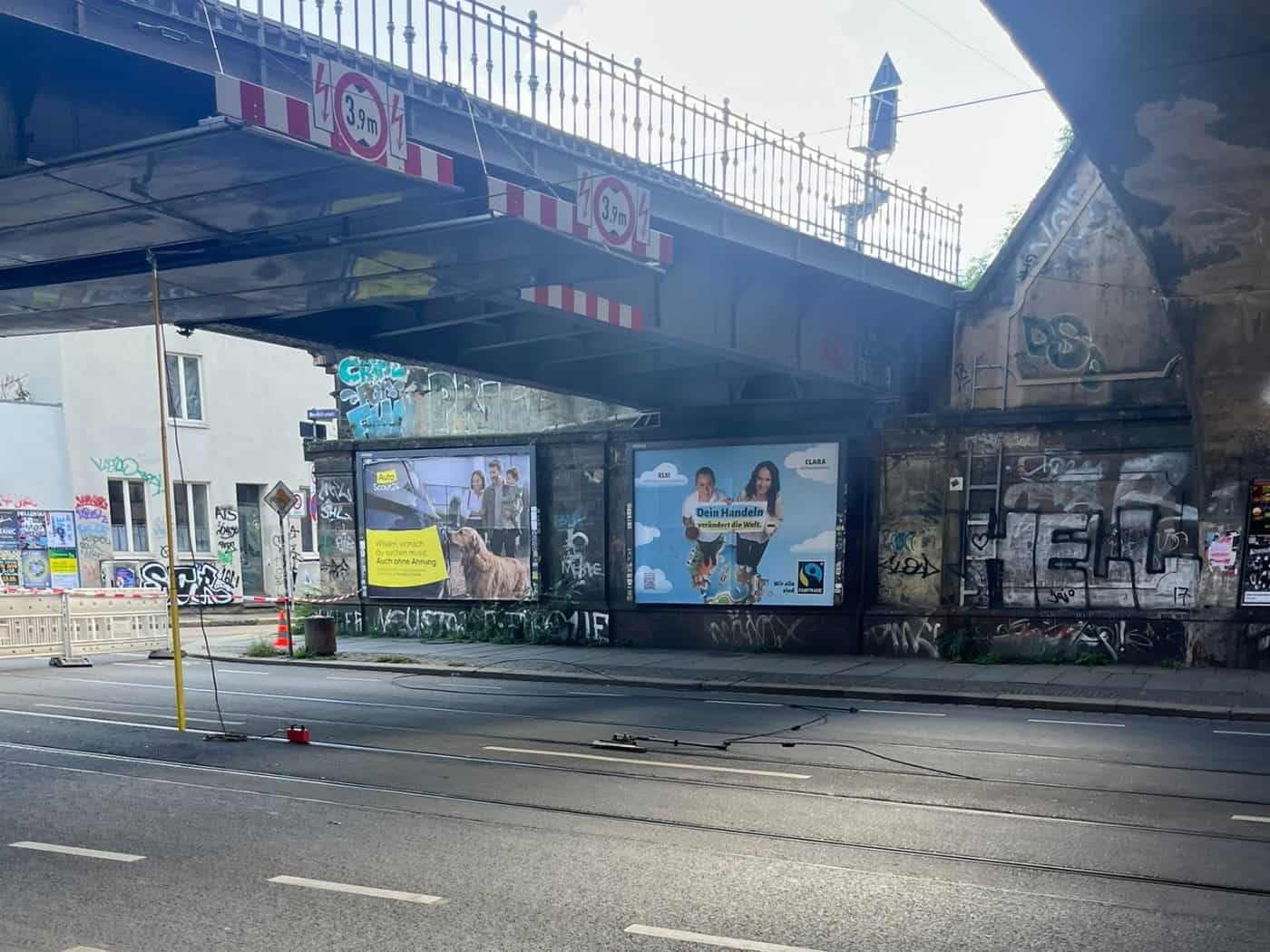 Ein herunterhängendes und auf dem Asphalt liegendes Kabel der Straßenbahn-Oberleitung unter einer dunklen Eisenbahnbrücke mit Werbeplakaten und Graffiti am Dresdner Bischofsweg.