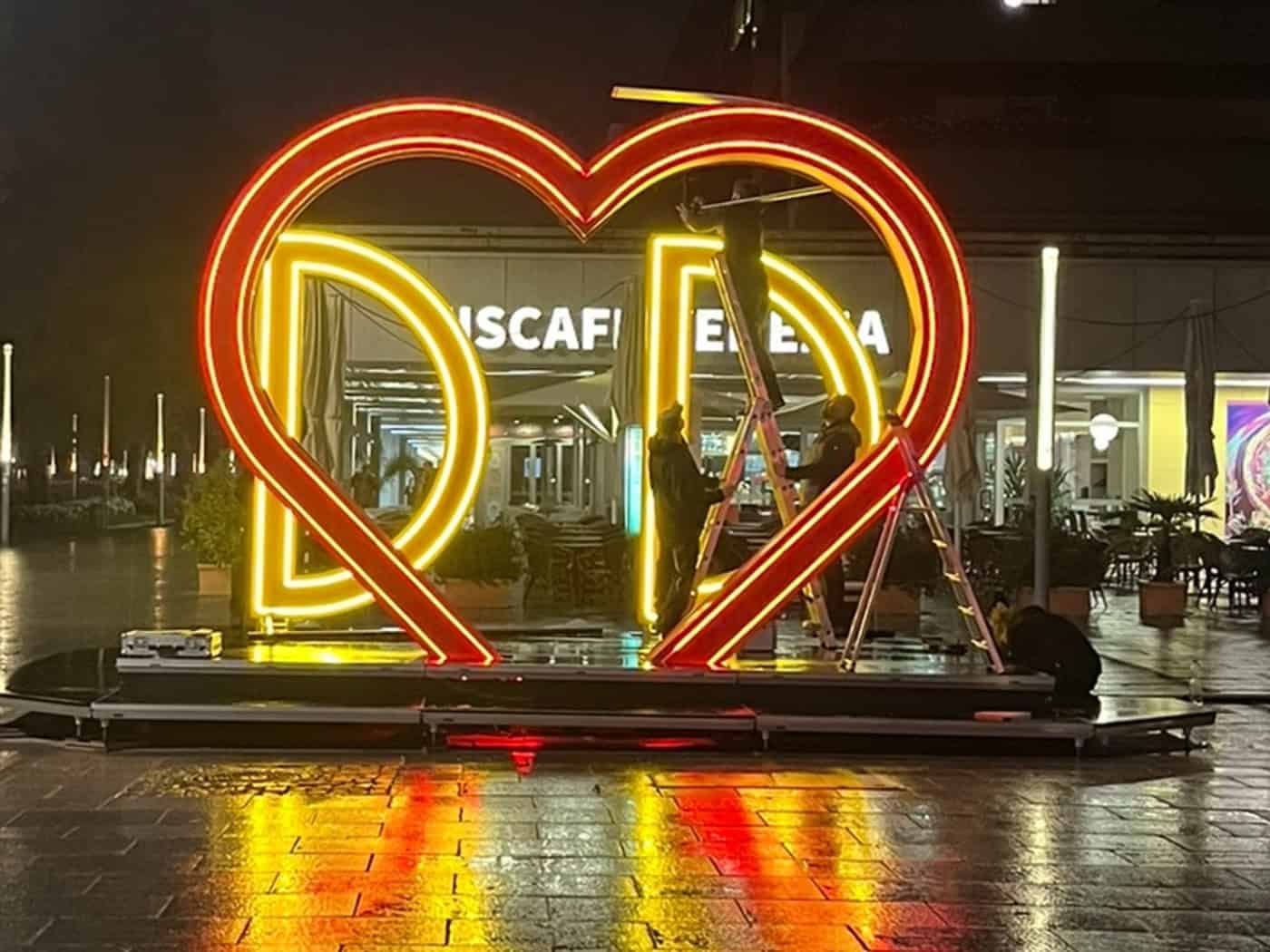 Ein groß, rot-gelb leuchtendes Neon-Herz mit den Buchstaben DD steht nachts auf dem nassen Pflaster der Dresdner Hauptstraße. Dahinter montieren Arbeiter die Installation vor dem Familienfest am Goldenen Reiter.