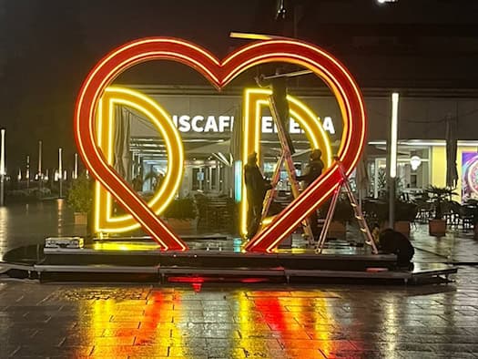 Ein groß, rot-gelb leuchtendes Neon-Herz mit den Buchstaben DD steht nachts auf dem nassen Pflaster der Dresdner Hauptstraße. Dahinter montieren Arbeiter die Installation vor dem Familienfest am Goldenen Reiter.