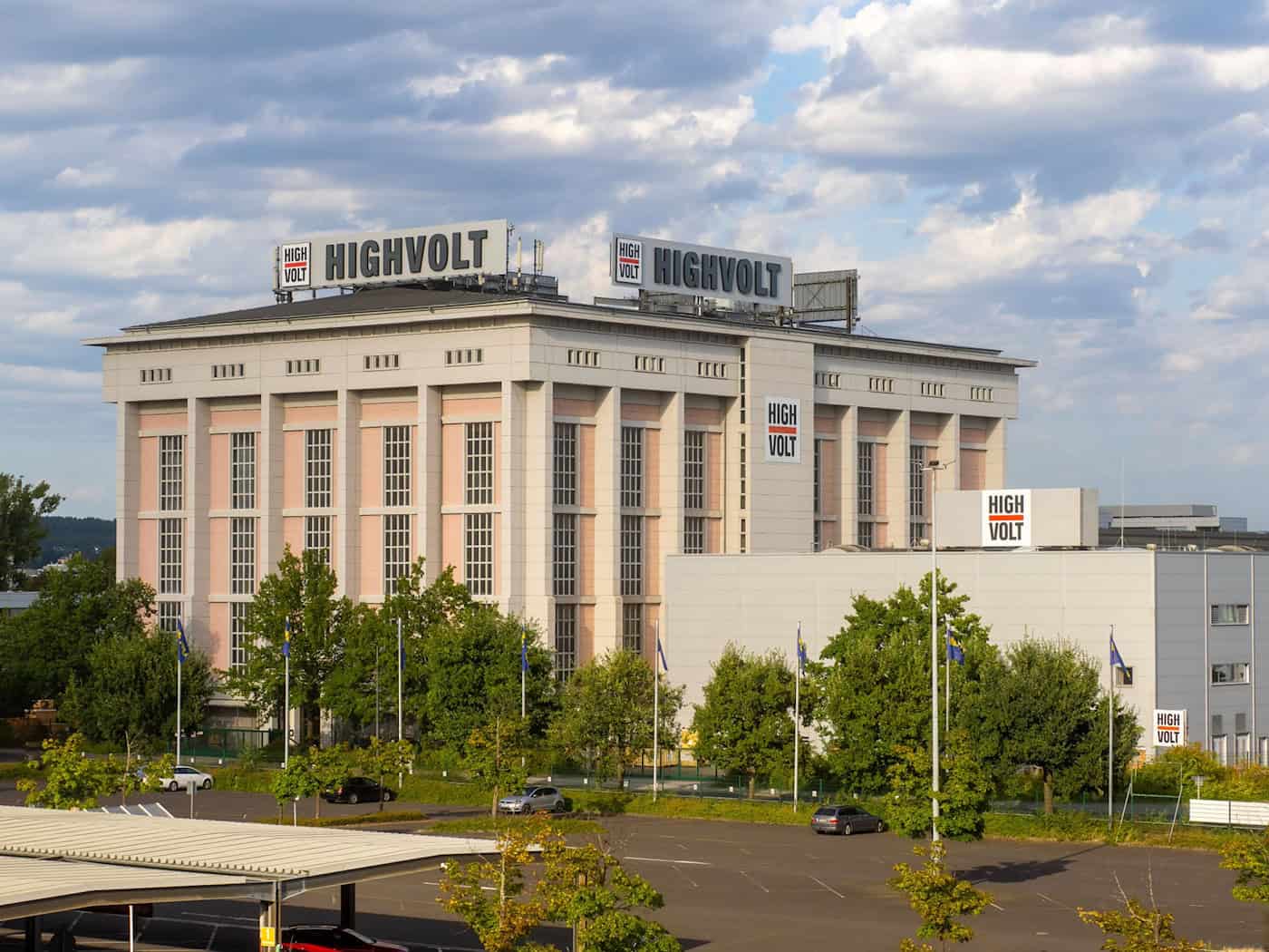Dresdner Hochspannungshalle der HIGHVOLT Prüftechnik mit neuen Logos Totale Aufnahme der imposanten, denkmalgeschützten Hochspannungshalle Dresden mit neuen HIGHVOLT-Schriftzügen auf dem Dach und an den Fabrikgebäuden vor leicht bewölktem Himmel.
