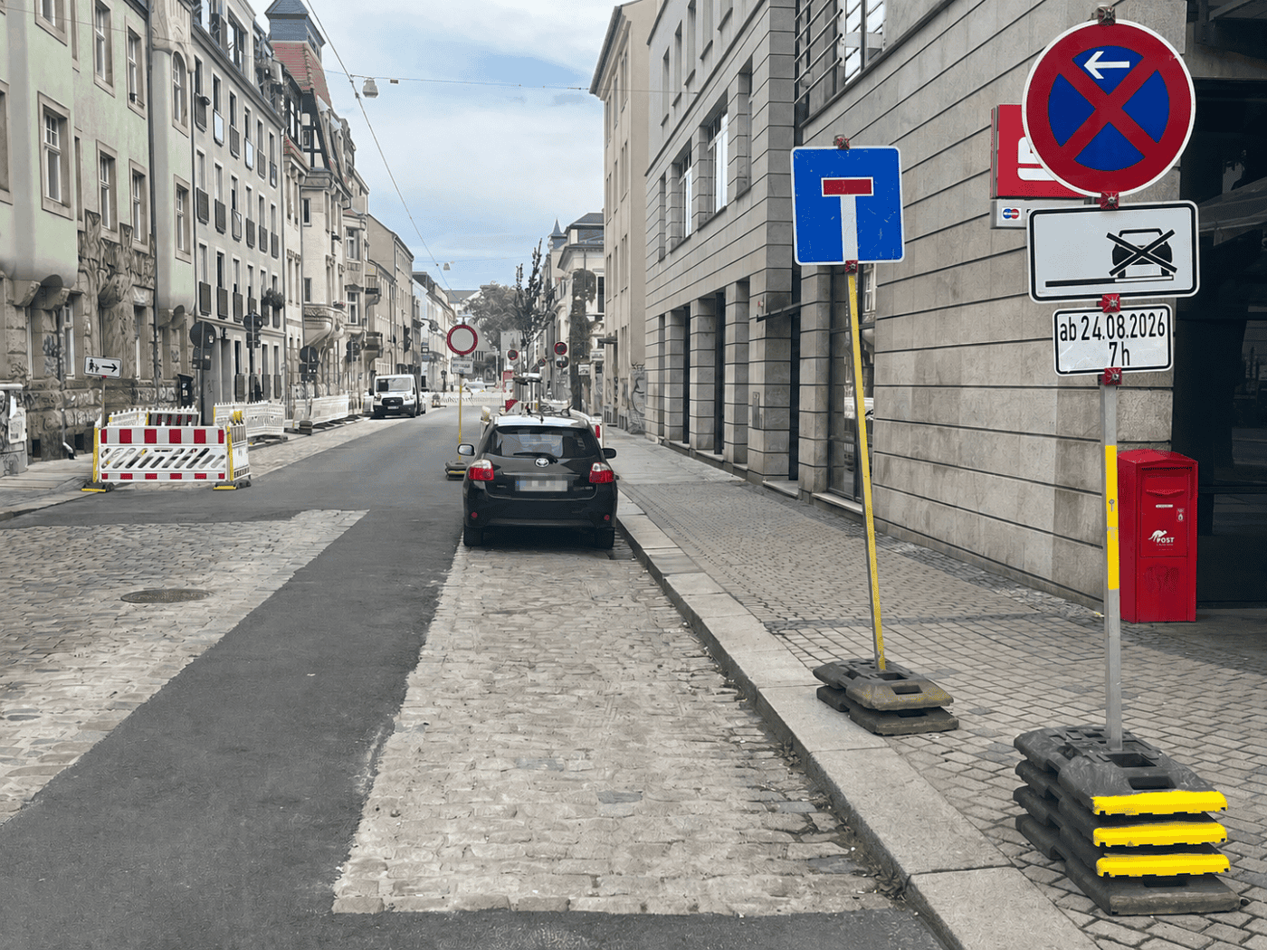 Blick in die Dresdner Katharinenstraße: Ein frisch gepflasterter Parkstreifen mit einem geparkten Auto, eingerahmt von Absperrschranken, Sackgassen- und Absperrschildern. Rechts auf dem Gehweg stehen ein roter Postbriefkasten und ein Halteverbotsschild.