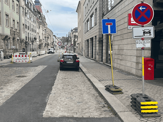 Blick in die Dresdner Katharinenstraße: Ein frisch gepflasterter Parkstreifen mit einem geparkten Auto, eingerahmt von Absperrschranken, Sackgassen- und Absperrschildern. Rechts auf dem Gehweg stehen ein roter Postbriefkasten und ein Halteverbotsschild.