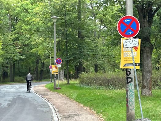 Grüner Straßenverlauf des Lothringer Wegs mit Bäumen und einem Radfahrer im Hintergrund. Im Vordergrund steht ein absolutes Halteverbotsschild mit dem Zusatzschild „ab 22.9.26 ab 7 Uhr“.