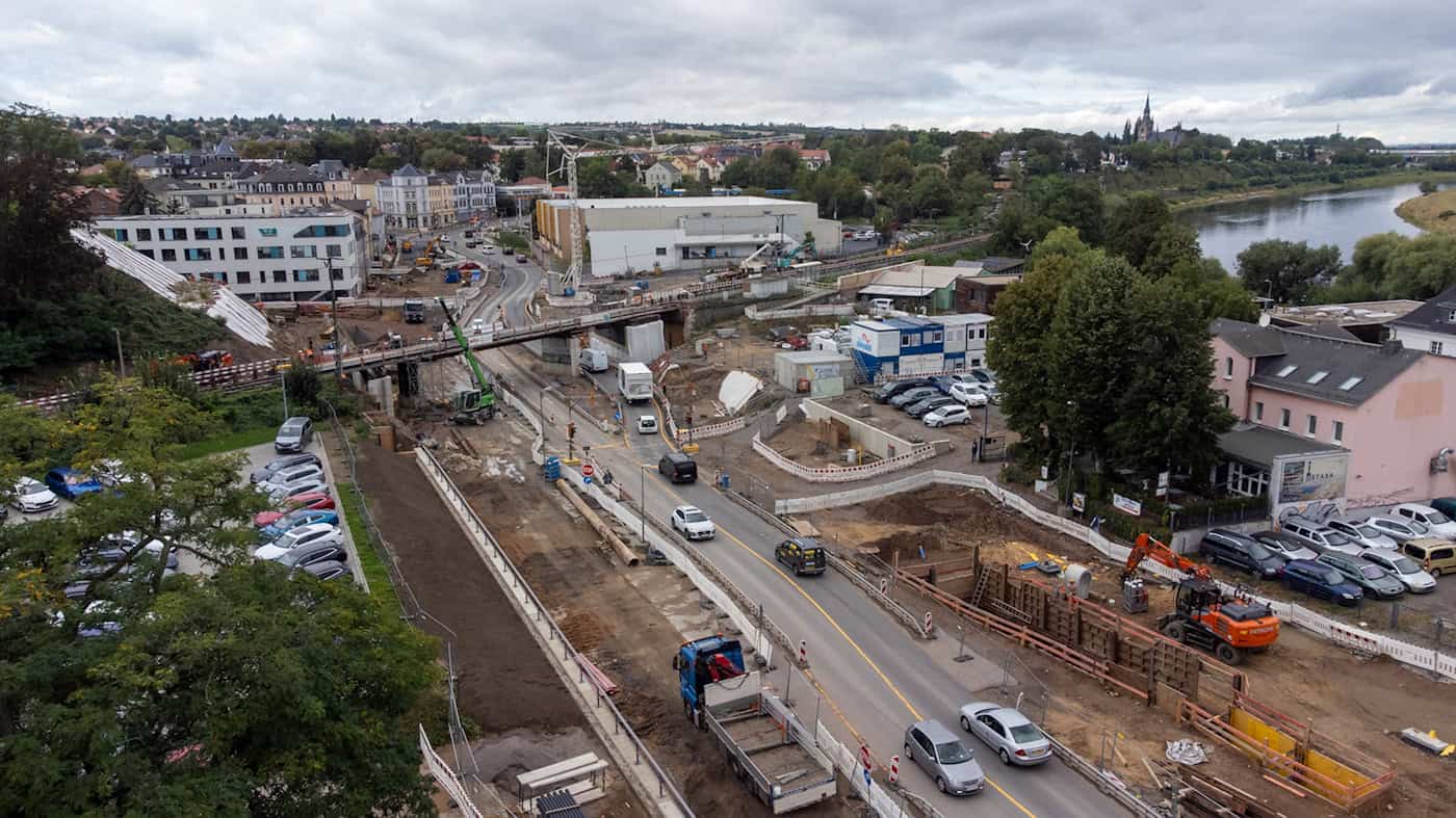 Luftaufnahme der Großbaustelle Hamburger Straße in Dresden nahe der Elbe Drohnenaufnahme einer langgestreckten Straßenbaustelle mit Baggern, Baugruben und verengter Fahrbahn. Rechts verläuft die Elbe, im Hintergrund sind Stadtteile und eine Eisenbahnbrücke zu sehen.