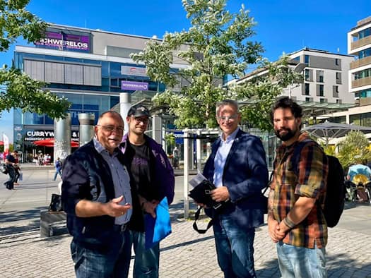 Vier Männer stehen draußen auf dem sonnigen Wiener Platz in Dresden: André Barth, Peter Henker mit Mütze, MdB Markus Reichel im Sakko und Sozialarbeiter Alexander Beuschel mit Rucksack (v.l.n.r.). Im Hintergrund ein Geschäftsgebäude.