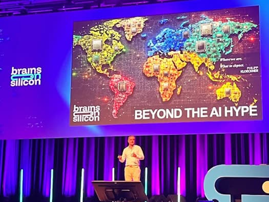 Tech analyst Philipp Klöckner stands on a conference stage lit by blue lights. The large screen behind him displays a colorful world map featuring computer chips, along with the titles “Brains on Silicon” and “BEYOND THE AI HYPE.”