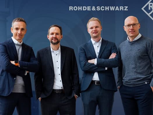 Vier Männer in Business-Kleidung stehen nebeneinander vor einem blauen Hintergrund mit dem Logo von Rohde & Schwarz: Thomas Bohne, Kai-Uwe Storek, Robert Wünsche und Steffen Bittner blicken in die Kamera.