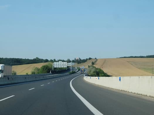 Autobahn mit Fahrzeugen zwischen Feldern unter blauem Himmel