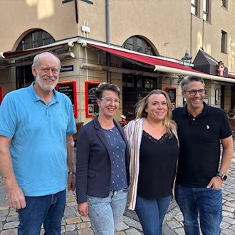 Vier Personen der Watzke-Geschäftsführung stehen lächelnd nebeneinander in einer Kopfsteinpflastergasse vor einer Gaststätte mit roter Markise. Links hängt ein blaues Straßenschild mit der Aufschrift „Münzgasse“ an der Gebäudewand.