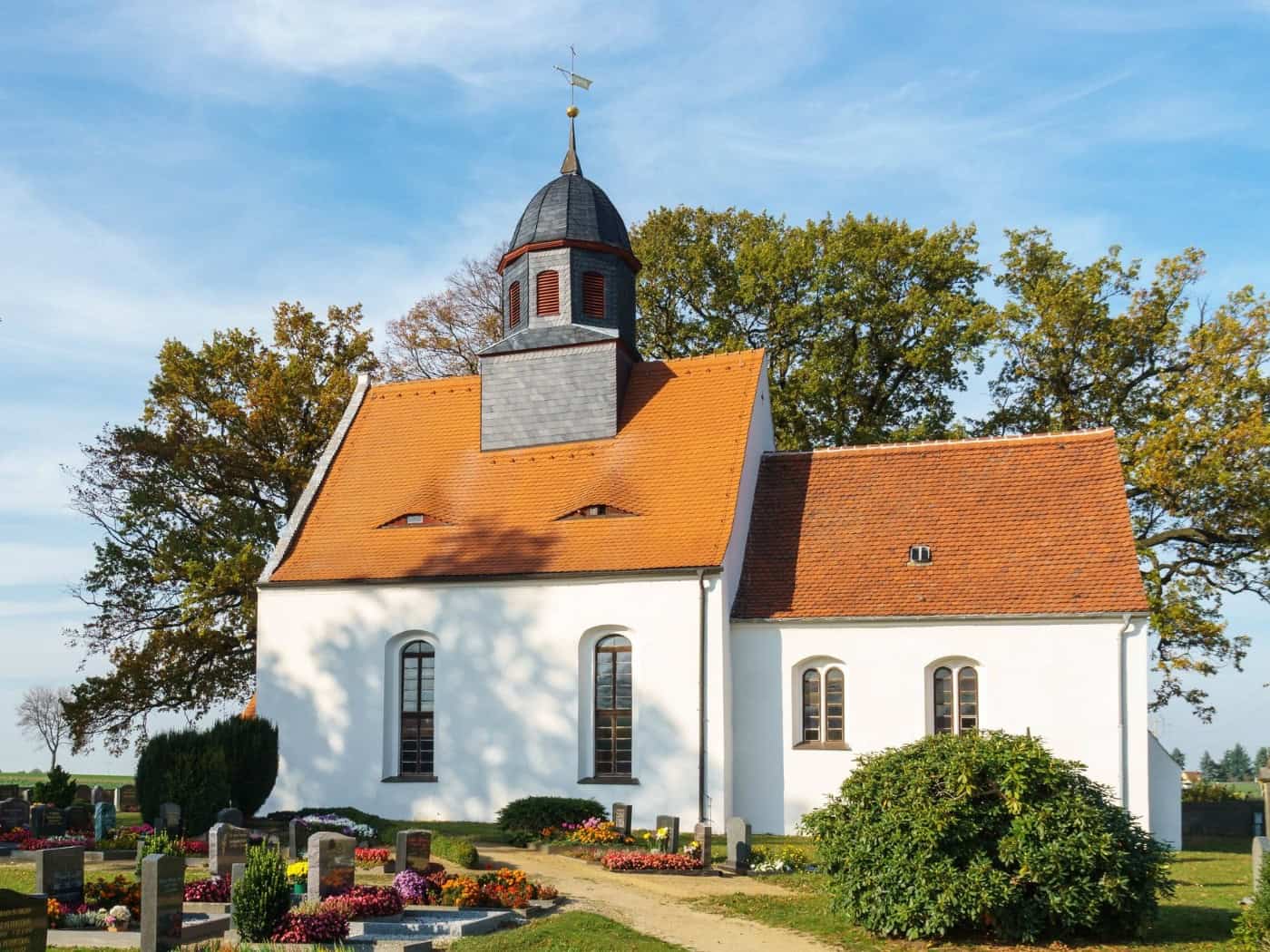 Weiße Dorfkirche mit rotem Ziegeldach und Dachreiter in Steinbach bei Moritzburg, davor der Friedhof