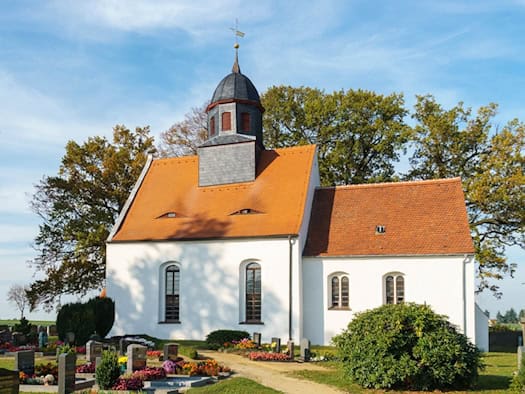 Weiße Dorfkirche mit rotem Ziegeldach und Dachreiter in Steinbach bei Moritzburg, davor der Friedhof