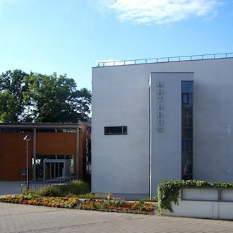 Modernes weißes Rathausgebäude in Coswig mit senkrechtem Schriftzug Rathaus, davor ein Blumenbeet