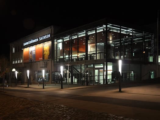 Beleuchtetes Theatergebäude mit großer Glasfront und Schriftzug Landesbühnen Sachsen bei Nacht