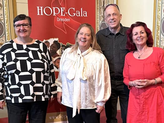 Vier lächelnde Personen stehen nebeneinander vor einem roten Banner der HOPE-Gala Dresden: Dr. Maria Decker in gemustertem Oberteil, Kathy Kelly in weißer Bluse, Stefan Hippler in dunklem Hemd und Viola Klein in einem knalligen pinken Kleid.