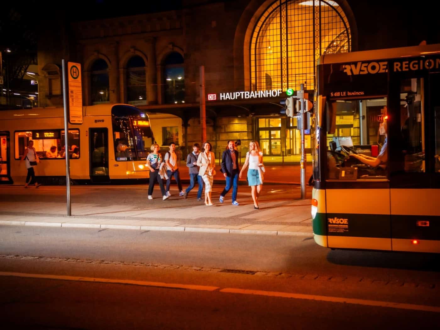Fahrgäste gehen nachts am Dresdner Hauptbahnhof von einer Straßenbahn zu einem Regionalbus.