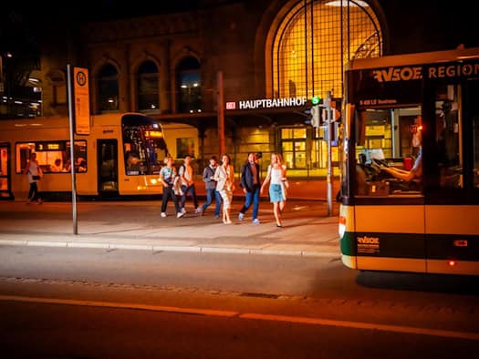 Fahrgäste gehen nachts am Dresdner Hauptbahnhof von einer Straßenbahn zu einem Regionalbus.