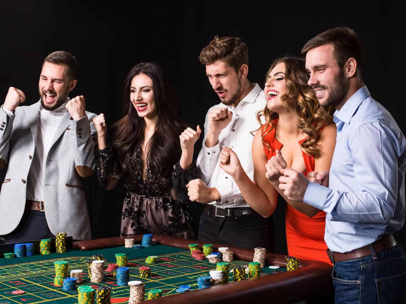 Fünf elegant gekleidete Personen feiern um einen Roulette-Tisch, auf dem Stapel von Spielchips liegen