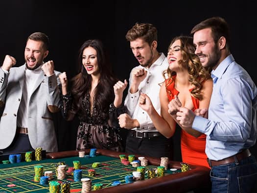 Fünf elegant gekleidete Personen feiern um einen Roulette-Tisch, auf dem Stapel von Spielchips liegen