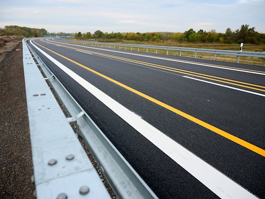 Neue, leere Autobahnfahrbahn mit gelben Baustellenmarkierungen und Leitplanke an einem bewölkten Herbsttag