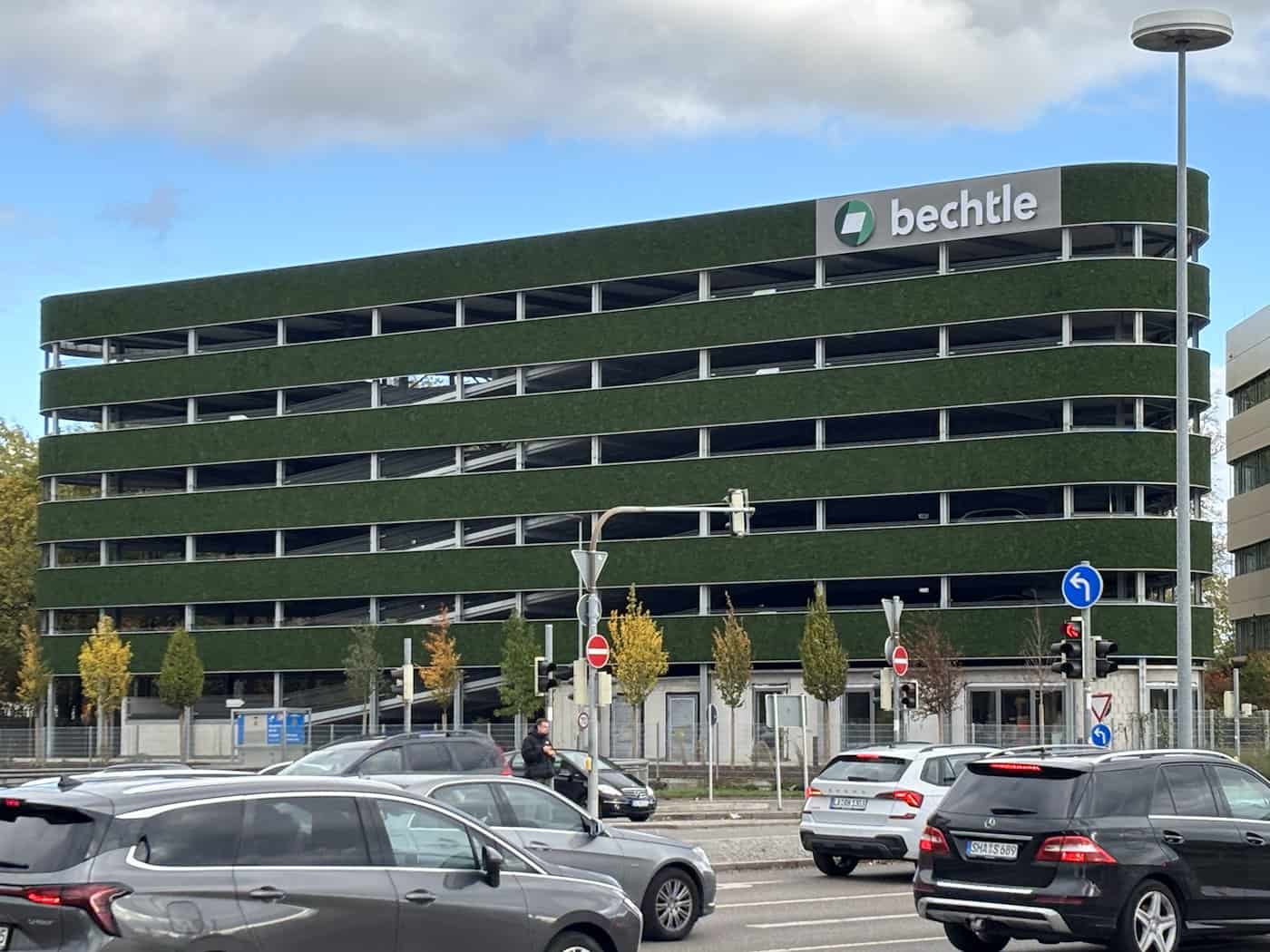 Gesamtaufnahme des langgestreckten, fünfstöckigen Parkhauses mit durchgehender grüner Moosfassade und dem Firmenschriftzug „bechtle“ auf dem Dach. Im Vordergrund verläuft eine Straße mit vorbeifahrenden Autos.