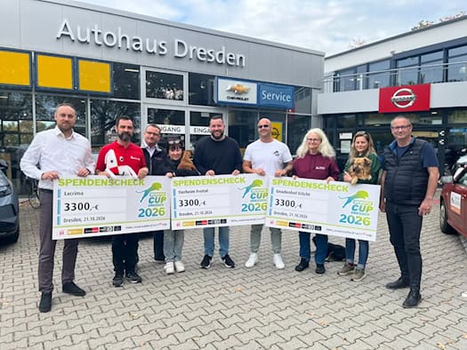 Neun Personen stehen mit drei großen Spendenschecks über jeweils 3.300 Euro und zwei Hunden vor dem Autohaus Dresden.