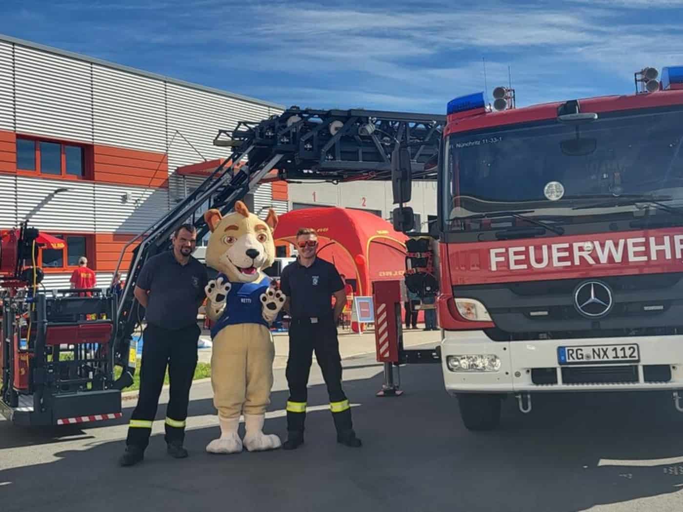 Feuerwehrleute mit einem Maskottchen vor Feuerwehrfahrzeugen beim Bevölkerungsschutztag in Glaubitz
