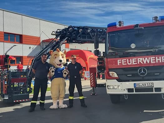 Feuerwehrleute mit einem Maskottchen vor Feuerwehrfahrzeugen beim Bevölkerungsschutztag in Glaubitz