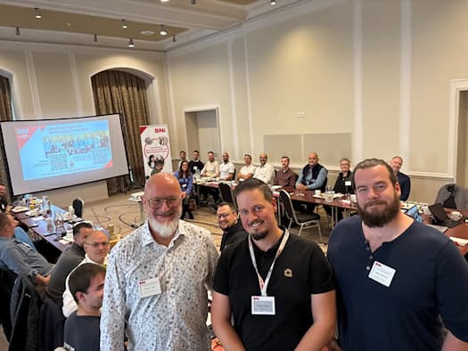 Drei Mitglieder des Dresdner BNI-Chapters „Konrad der Große“ stehen im Vordergrund beim Frühbucher-Treffen; im Hintergrund versammelte Unternehmer an gedeckten Tischen im Hotel.