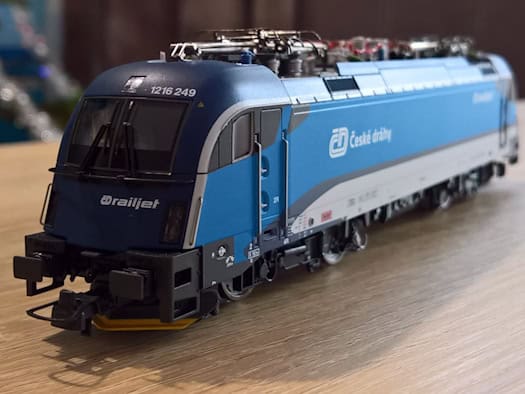 Symbolbild: Ein blau-graues Modell einer ČD-Elektrolokomotive der Tschechischen Bahnen mit der Aufschrift „Railjet“ steht auf einem Holztiisch vor unscharfem Hintergrund.