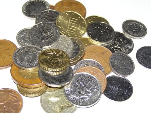 Münzen verschiedener Währungen, darunter tschechische Kronen und Euro, auf einer weißen Fläche.