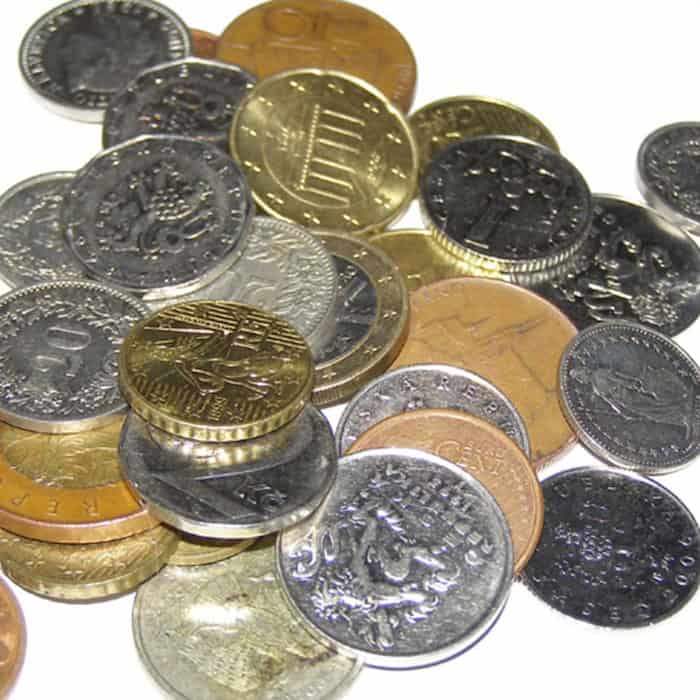 Münzen verschiedener Währungen, darunter tschechische Kronen und Euro, auf einer weißen Fläche.