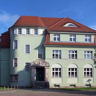 Hellgrünes Gebäude mit rotem Dach und Rundturm in der Karrasstraße 3 in Coswig