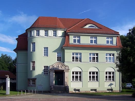 Hellgrünes Gebäude mit rotem Dach und Rundturm in der Karrasstraße 3 in Coswig
